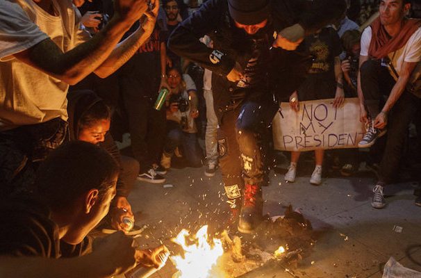 Supporters of Hillary Clinton, along with other groups of fringe radical leftists, burn American flags during protests against the election of President-Elect Donald J. Trump.