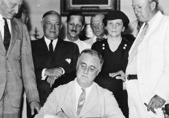 President Franklin D. Roosevelt signs the Social Security Act of 1935 on August 14, 1935. Present at the signing was Rep. Robert Doughton (D-NC); unknown person in shadow; Sen. Robert Wagner (D-NY); Rep. John Dingell (D-MI); Rep. Joshua Twing Brooks (D-PA); the Secretary of Labor, Frances Perkins; Sen. Pat Harrison (D-MS); and Rep. David Lewis (D-MD).