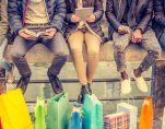 Group of friends sitting outdoors with shopping bags; several people holding smartphones and tablets. (Photo: AdobeStock/ OneInchPunch/PPD)