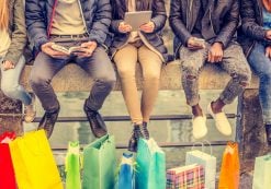 Group of friends sitting outdoors with shopping bags; several people holding smartphones and tablets. (Photo: AdobeStock/ OneInchPunch/PPD)