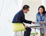 A man and woman discuss business collaborating on an online project using a touchpad tablet in a modern office space. (Photo: AdobeStock)