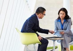 A man and woman discuss business collaborating on an online project using a touchpad tablet in a modern office space. (Photo: AdobeStock)