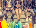 Group of friends sitting outdoors with shopping bags; several people holding smartphones and tablets. (Photo: AdobeStock/ OneInchPunch/PPD)