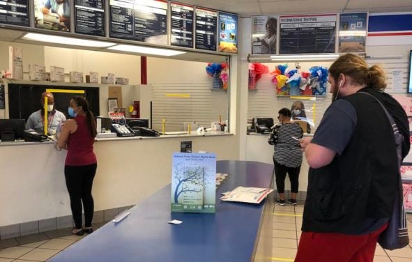 United States Postal Service (USPS) workers don face masks and gloves behind plexiglass at the USPS location on N. Main in Gainesville, Fla., during the coronavirus (COVID-19) pandemic. (Photo: People's Pundit Daily/PPD)