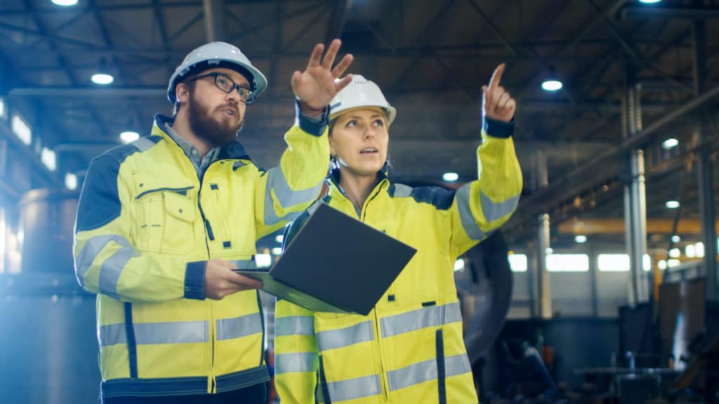 Two engineers — one male and one female — in a manufacturing factory discussing operations in industrial production. (Photo: AdobeStock)