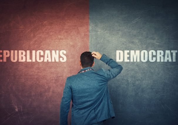 A puzzled businessman and a split wall with Republicans and Democrats written on red and blue sides to illustrate the choice between parties in elections. (Photo: AdobeStock)