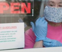 With cautious optimism a small business owner wearing a face mask and disposable gloves posts safety rules as she reopens her store after the coronavirus (COVID-19)shutdown. (Photo: AdobeStock/JHDT Productions)