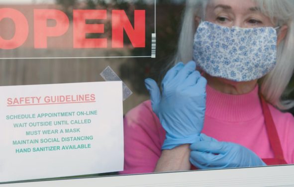 With cautious optimism a small business owner wearing a face mask and disposable gloves posts safety rules as she reopens her store after the coronavirus (COVID-19)shutdown. (Photo: AdobeStock/JHDT Productions)