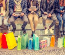 Group of friends sitting outdoors with shopping bags; several people holding smartphones and tablets. (Photo: AdobeStock/ OneInchPunch/PPD)