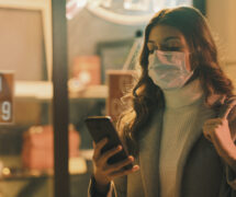 Shop closed due to coronavirus outbreak and woman looking at her mobile device and wearing a surgical mask. (Photo: AdobeStock)